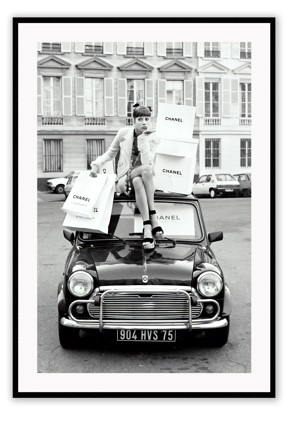 A black and white vintage fashion wall art with a lady holding Chanel shopping bags riding on vintage car Fiat in European city. 