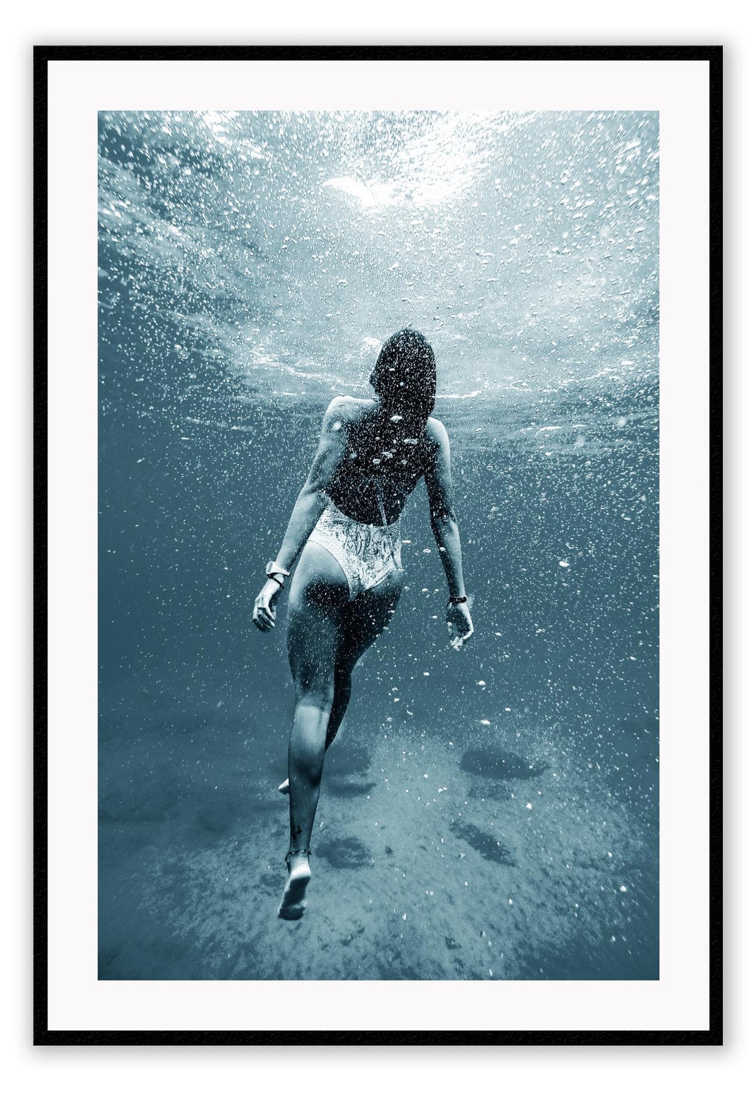 Photography of woman swimming in blue sea water looking up towards the surface pointed toes bubbles 