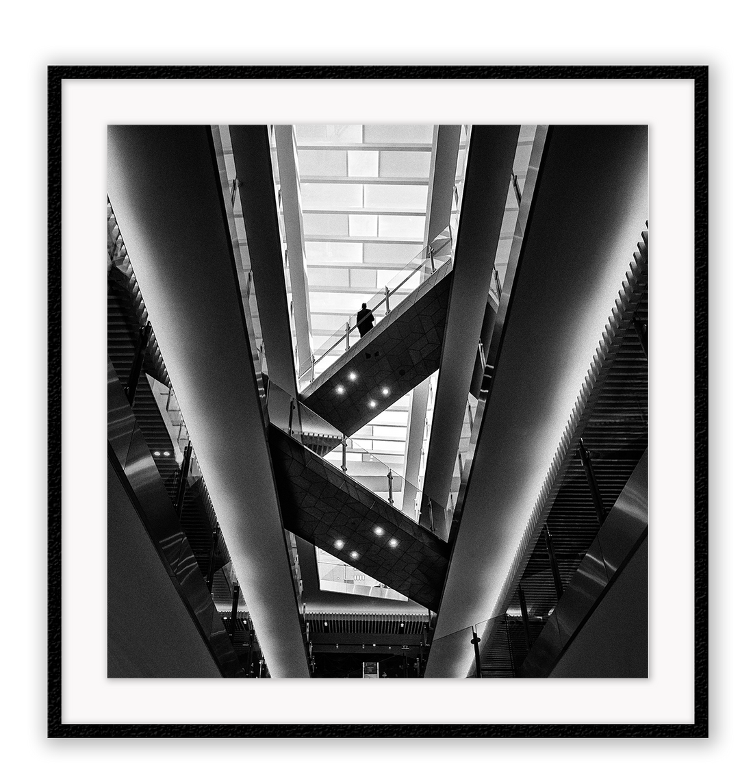 Photography print in black and white with man standing on accending escalator.